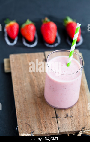 Frullato di fragole con paglia a strisce e fragole intere su sfondo scuro Foto Stock