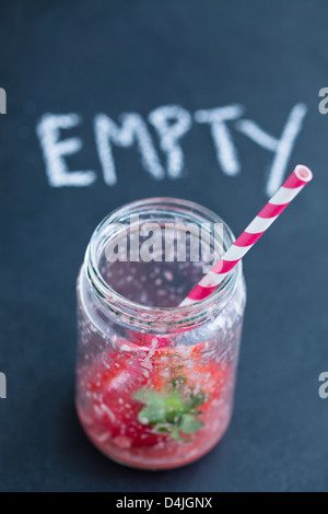 Vuoto frullato fragole vetro rigato con paglia e chalk testo su sfondo scuro Foto Stock