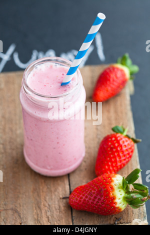 Frullato di fragole con paglia a strisce e fragole intere su legno portagiornali Foto Stock