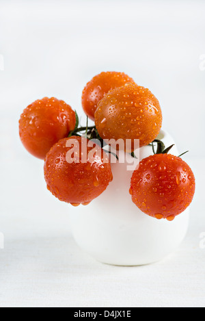 Freschi pomodori ciliegia in un vaso bianco su uno sfondo luminoso Foto Stock