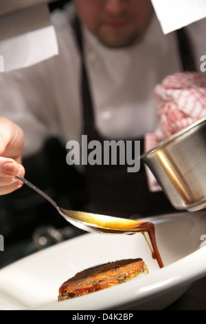 Lo Chef drizzling gravy sopra una patata e il segnale di PEA Röstinchen in ristorante nel Regno Unito. Foto Stock