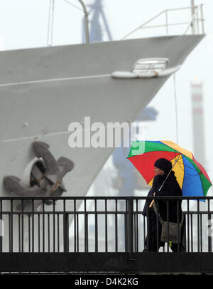 Una donna cammina passato grigio di una nave con il suo ombrello coloratissimo sotto la pioggia battente vicino al lungomare a Amburgo?s horbour, Germania, 23 marzo 2009. I meteorologi di predire la pioggia, vento e freddo con temperature comprese tra 5 e 7 gradi Celsius a prevalere i prossimi giorni. Foto: Marcus Brandt Foto Stock