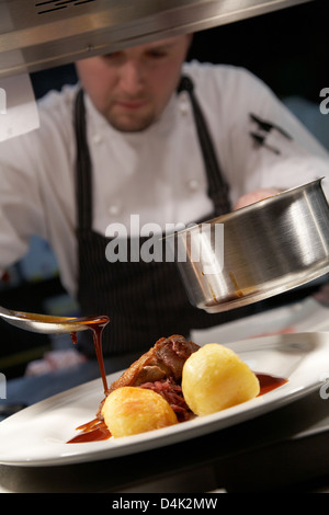 Lo Chef drizzling oltre il sugo di anatra arrosto e patate in un ristorante nel Regno Unito. Foto Stock