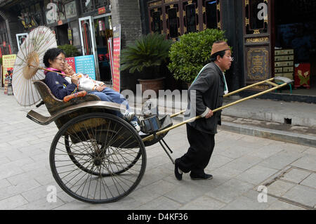 Un rickshaw driver porta i passeggeri attraverso le antiche strade di Pingyao, una delle poche città cinesi con una intatta cinta muraria, in Cina, 05 ottobre 2008. La città storica della dinastia Ming (1368-1644) si trova a circa 500 km a sud-ovest di Pechino. Di Pingyao è un ex centro finanziario e casa del primo cinese discout house nel 1824. Templi storici, case e strade rendono Foto Stock