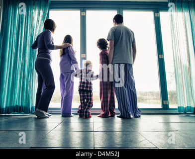 Famiglia in pigiama a guardare fuori dalla finestra Foto Stock