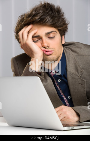 Ritratto di sonno imprenditore oberato di lavoro davanti al suo computer portatile al lavoro. Foto Stock