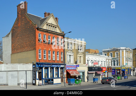 La Canning Town di vecchi edifici nella principale strada dello shopping con cestini della spazzatura fuori dei negozi in attesa di svuotamento Foto Stock