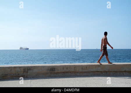 L'Avana, Cuba, un uomo passa sul muro di pietra lungo il Malecon Foto Stock