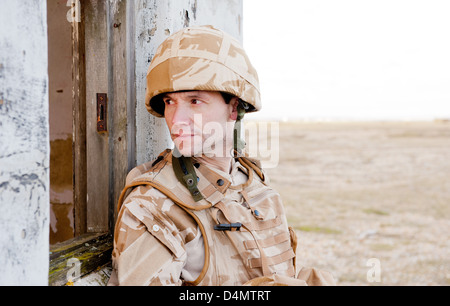 Soldato britannico indossa desert camouflage uniforme e guardando attraverso la finestra di un edificio abbandonato. Foto Stock