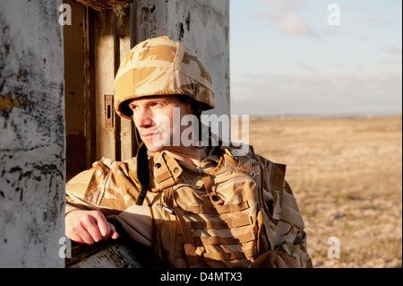 Soldato britannico indossa desert camouflage uniforme e guardando attraverso la finestra di un edificio abbandonato. Foto Stock