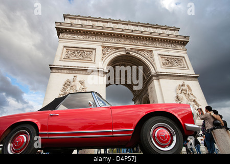 Coppia giapponese fotografando l'Arc de Triomphe a Parigi; rosso Mercedes veterano auto di fronte all'Arco di Trionfo Foto Stock