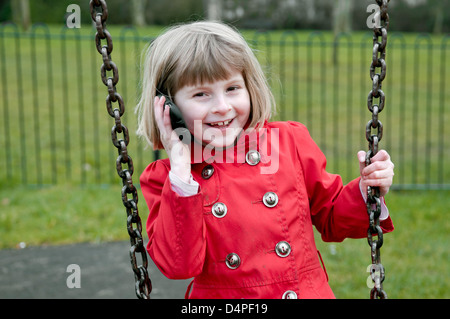 8 anno vecchia ragazza caucasica ridendo e parlando al telefono cellulare mentre dire sull'altalena. Foto Stock