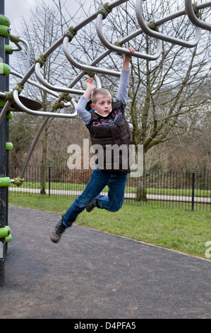 I giovani di 10 anni ragazzo caucasico oscillare attraverso il telaio di arrampicata nel parco in Bristol, Regno Unito Foto Stock