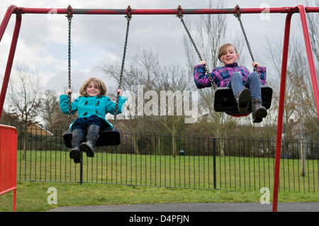 Due di 8 anni ragazze caucasica divertirsi giocando sulle altalene nel parco in Bristol, Regno Unito Foto Stock