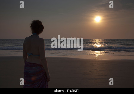 Una donna si affaccia al mare come il sole tramonta nel pomeriggio. Impostare su Arossim Beach, a sud di Goa, India. Foto Stock