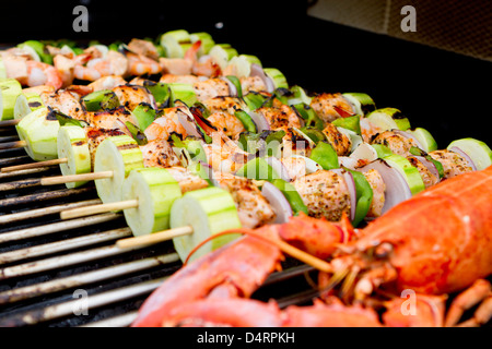 Salmone e spiedini di vegetali e di aragosta sono sul barbecue. Foto Stock