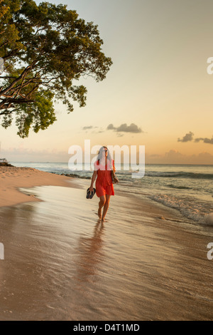 Una donna cammina lungo la spiaggia al tramonto, vicino a Holetown, parrocchia di Saint James, Barbados Foto Stock