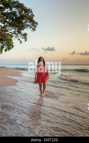 Una donna cammina lungo la spiaggia al tramonto, vicino a Holetown, parrocchia di Saint James, Barbados Foto Stock