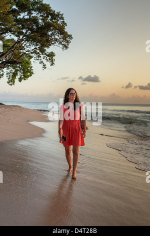 Una donna cammina lungo la spiaggia al tramonto, vicino a Holetown, parrocchia di Saint James, Barbados Foto Stock