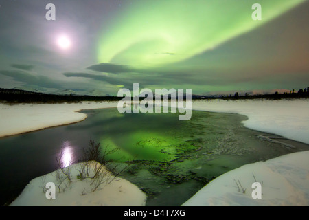 Aurora Boreale e luna piena impostazione su una montagna e creek dal pesce di lago, Whitehorse, Yukon, Canada. Foto Stock