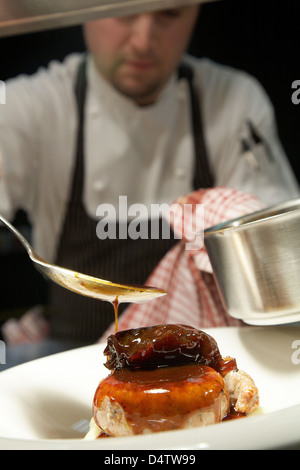 Lo Chef drizzling una salsa sopra un salsicce Cumberland con un fagiolo pisello e la salsa in un ristorante nel Regno Unito. Foto Stock