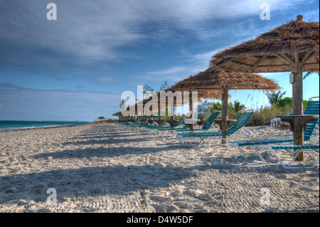 Ombrelloni e sedie a sdraio in spiaggia sotto un cielo blu Foto Stock