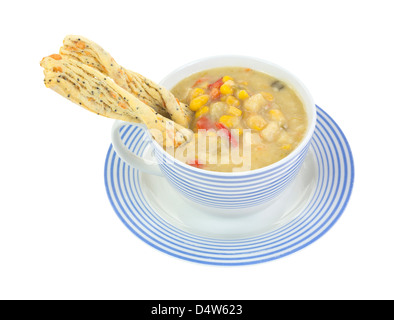 Una spessa chowder di mais, patate e peperoni rossi tagliati a strisce blu tazza e piattino con twisted cracker inserito nella zuppa. Foto Stock