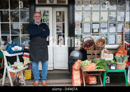 La Moulton village memorizza un tradizionali magazzini generali e ufficio postale in Suffolk REGNO UNITO con il negoziante in piedi al di fuori. Foto Stock