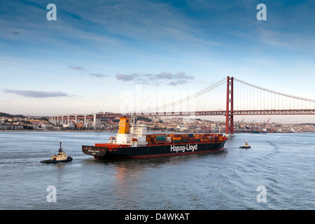 Lisbona, Portogallo. Una nave portacontainer con due rimorchiatori, teste per il ponte di Salazar. Chiamato anche 25APRILE Bridge e il Tago Foto Stock