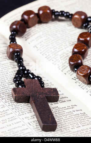 I grani del rosario e croce giacente su una pagina aperta della bibbia. Foto Stock