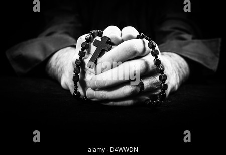 Mani tenendo i grani del rosario e croce pregando. Foto Stock