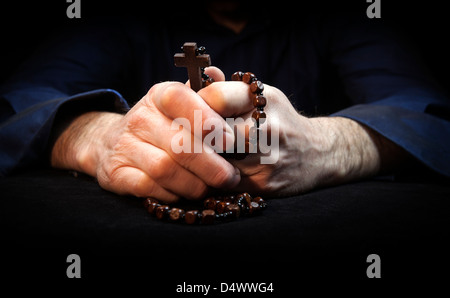 Mani tenendo i grani del rosario e croce pregando. Foto Stock