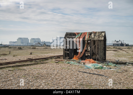 Il vecchio pescatore di legno la capanna con un impianto ad energia nucleare in background, Dungeness, Kent, England, Regno Unito Foto Stock