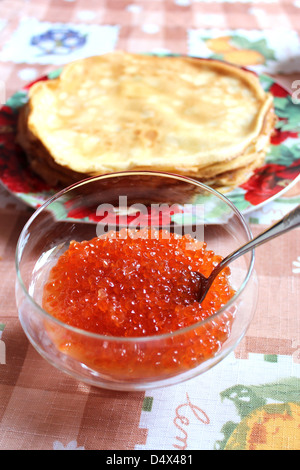 Caviale rosso in una piastra con il cucchiaio e le frittelle su uno sfondo Foto Stock