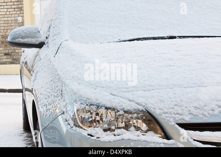 Il cofano anteriore e le luci delle auto europee rivestita di uno strato di neve fresca durante una dura stagione invernale Foto Stock