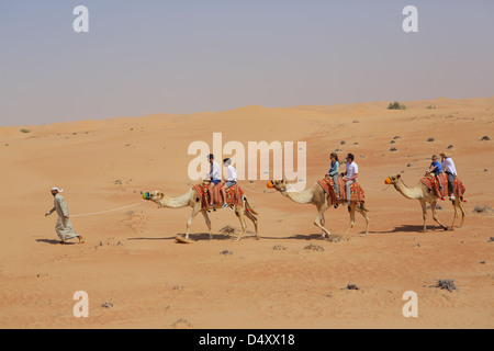 I turisti a cavallo di cammelli nel deserto, Dubai, Emirati Arabi Uniti Foto Stock