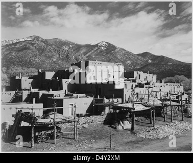 La fotografia di Ansel Adams del 1941 cattura una vista completa di Taos Pueblo, un monumento storico nazionale nel New Mexico, con montagne sullo sfondo, che mettono in risalto la bellezza culturale e naturale del sito. Foto Stock