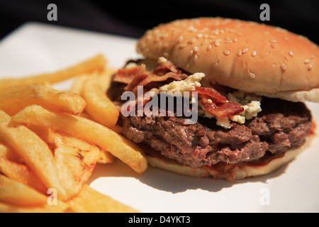 La pancetta e formaggio blu hamburger con patatine fritte su una piastra bianca Foto Stock