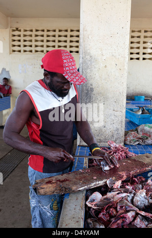 Pescatore locale per l'eviscerazione e la pulizia di teste di pesce al porto mercato in Micoud, St Lucia Foto Stock