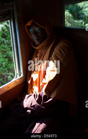 Un monaco buddista, ben confezionato contro il freddo, dozes su la mattina presto in treno da Mandalay a laschio in Myanmar. Foto Stock