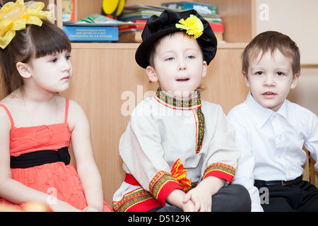 Carino ragazzo russo in abiti tradizionali in asilo nido seduti sulle sedie in aula. La Russia Foto Stock