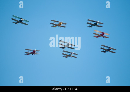 Un gruppo di otto vintage bi-aerei volare in formazione, visto da sotto contro un cielo blu chiaro. Foto Stock