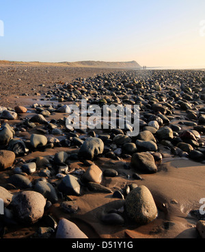 Due figure distanti a piedi in un dolce tramonto su uno sperone foreshore a Ballaugh nell'Isola di Man Foto Stock
