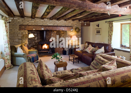 Un cottage accogliente soggiorno con stufa a legna i muri in pietra e travi a soffitto caratteristiche. Foto Stock