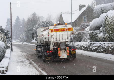 Nevica pesantemente durante la magia del freddo, nevoso inverno meteo & consiglio gritter carro (con Snow Plough) è la guida lungo, deselezionando la strada principale che attraversa il villaggio, spargimento sale di roccia sulla superficie il fuggitivo - Hawksworth, West Yorkshire, Inghilterra, Regno Unito. Foto Stock