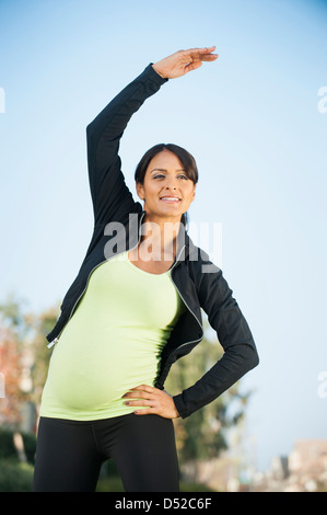 Incinta donna ispanica stretching all'aperto Foto Stock