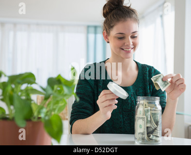 Ragazza ispanica mettere il denaro nel vaso di risparmio Foto Stock