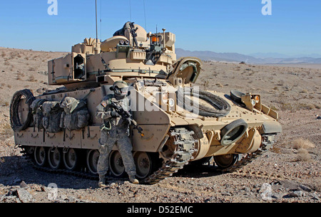 Un US Army soldier prende il coperchio accanto a un M2 Bradley di combattimento della fanteria veicolo durante una decisa azione di formazione presso il Centro Nazionale di Allenamento Gennaio 19, 2013 a Fort Irwin, CA. Foto Stock