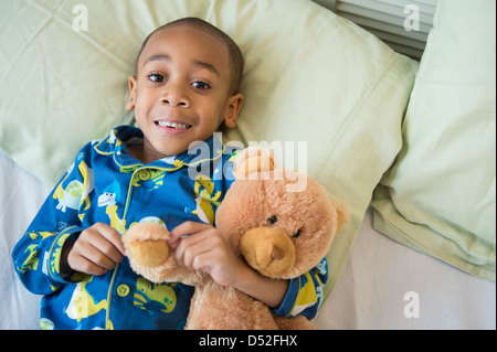 African American boy abbracciando Teddy bear a letto Foto Stock