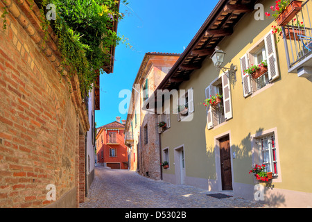 Stretta viuzza acciottolata tra il vecchio muro di mattoni e case colorate nella piccola città di Guarene in Piemonte, Italia settentrionale. Foto Stock